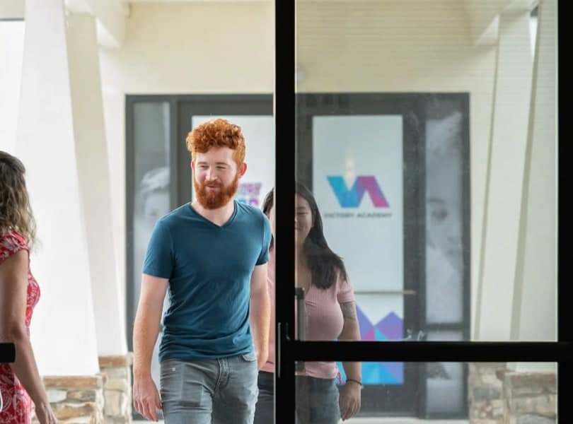 Three people walking in through the glass front doors of Victory Church.
