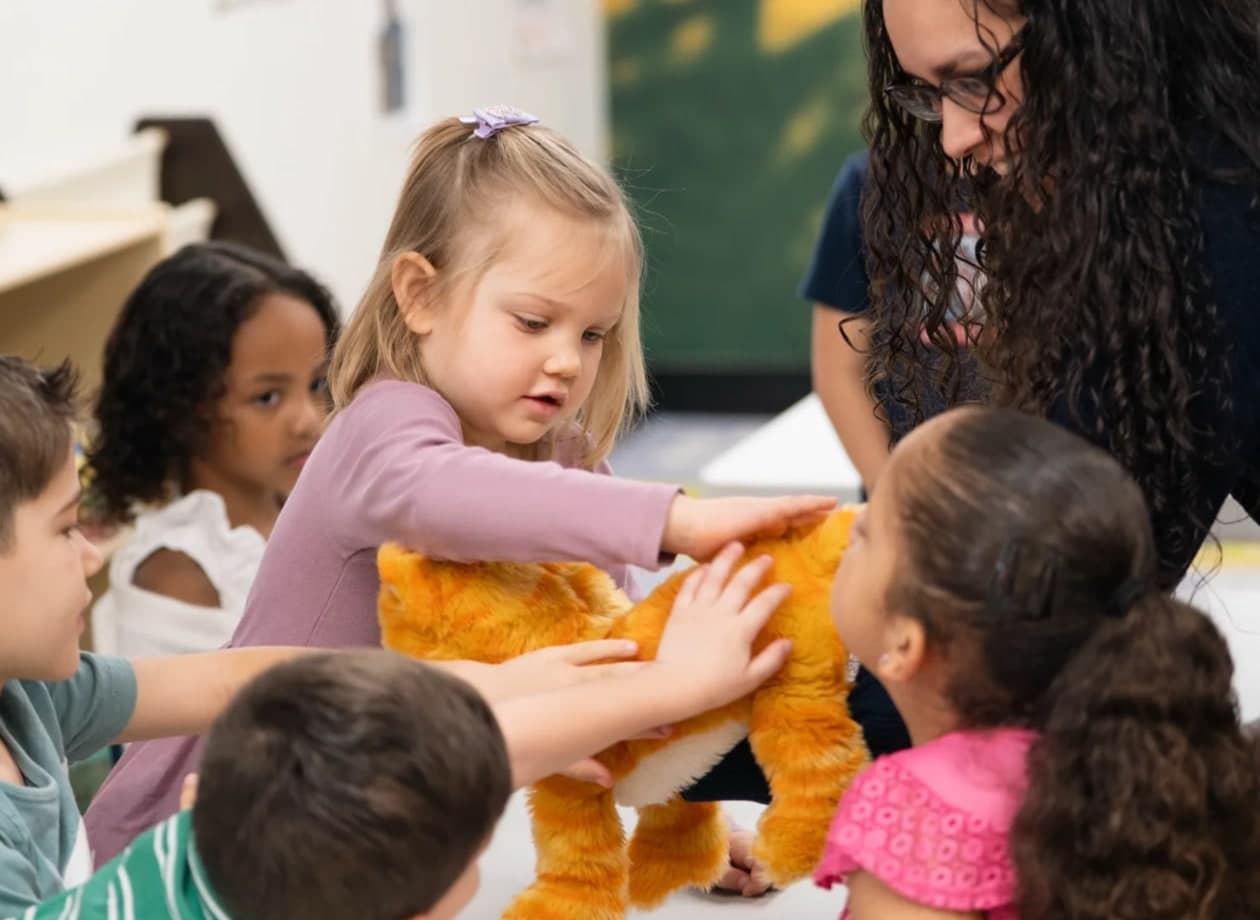 Young children gathered around a stuffed toy with a leader in Victory Kids.